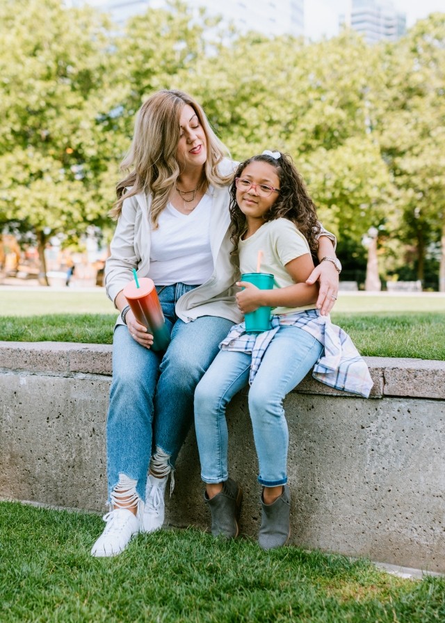 A mother sits at the park with her arm around her daughter