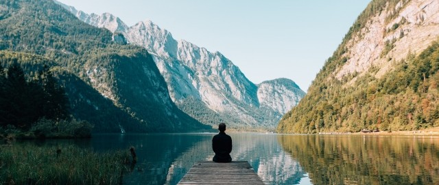 A person is sitting on a boat dock in the mountains.