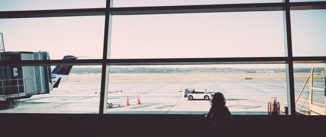 A young girl is looking out the window at the airport