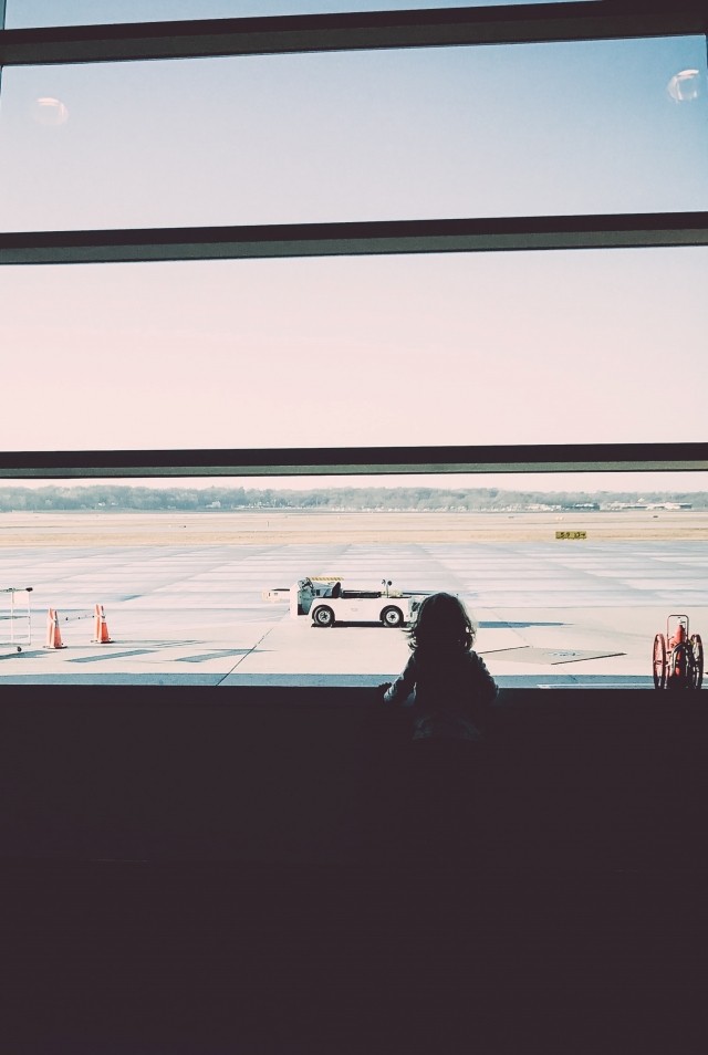 A young girl is looking out the window at the airport